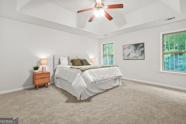 carpeted bedroom with a tray ceiling, baseboards, and ceiling fan