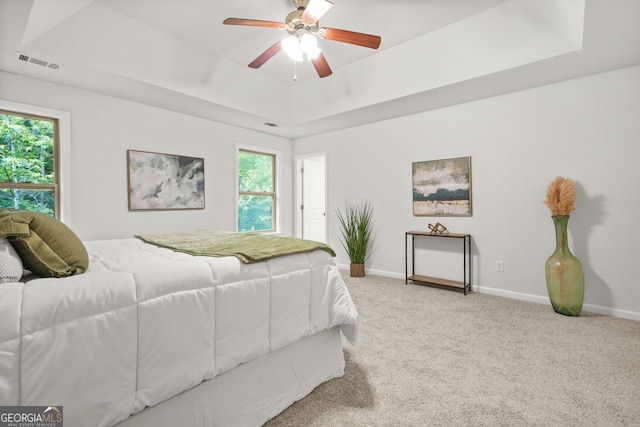 carpeted bedroom featuring a raised ceiling, multiple windows, baseboards, and ceiling fan