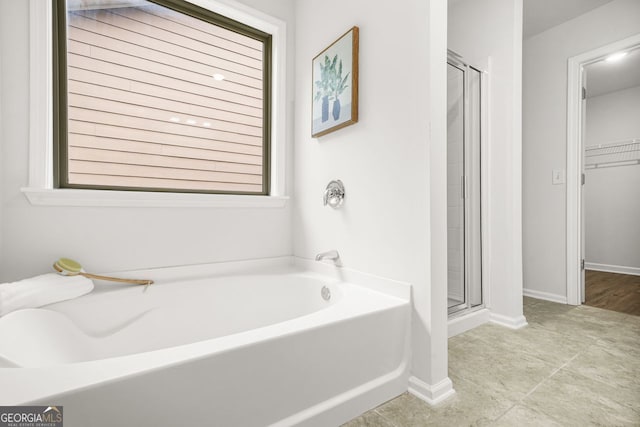 bathroom with a shower stall, a garden tub, a spacious closet, and baseboards