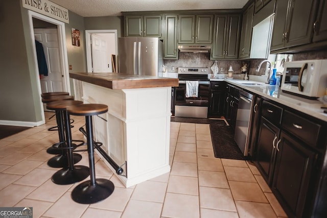 kitchen featuring appliances with stainless steel finishes, under cabinet range hood, a sink, wooden counters, and backsplash