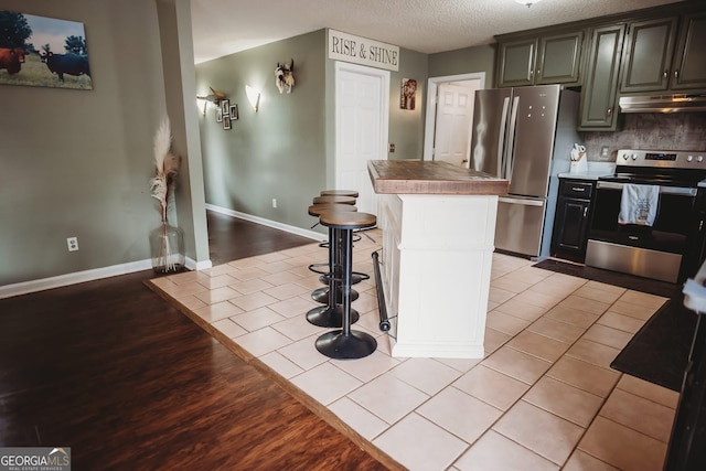 kitchen featuring stainless steel appliances, under cabinet range hood, a center island, a textured ceiling, and tasteful backsplash