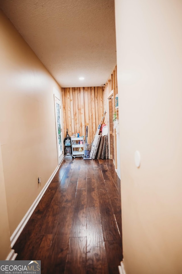 hall featuring dark wood-type flooring, a textured ceiling, baseboards, and wood walls