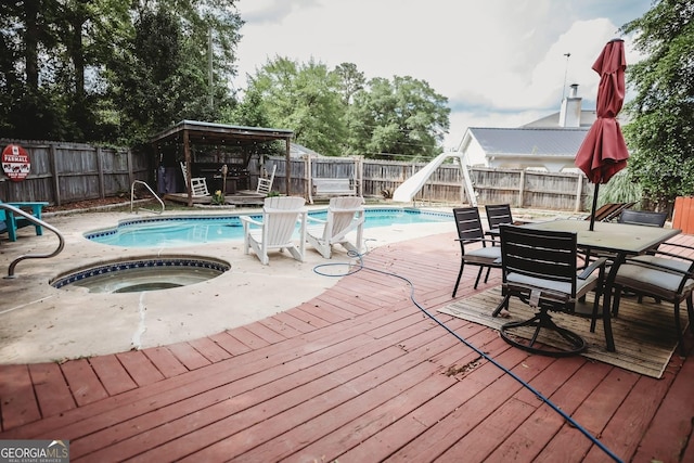 view of pool featuring an in-ground hot tub, a deck, a water slide, a fenced backyard, and outdoor dining area