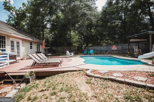 view of pool featuring a water slide, french doors, a wooden deck, and a fenced backyard