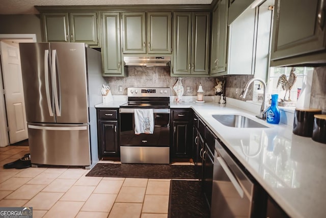 kitchen with appliances with stainless steel finishes, under cabinet range hood, a sink, green cabinets, and light countertops