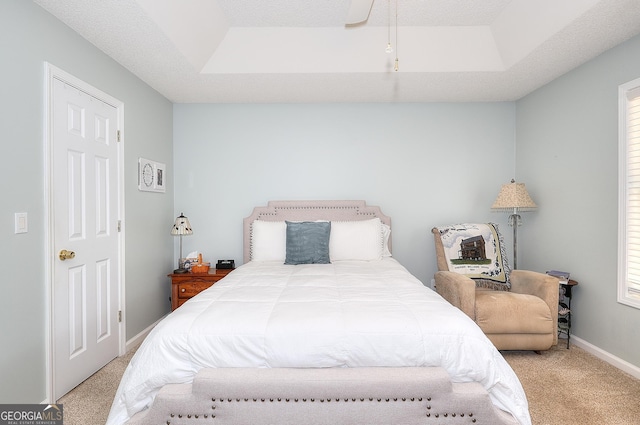 bedroom featuring carpet floors, a tray ceiling, baseboards, and multiple windows