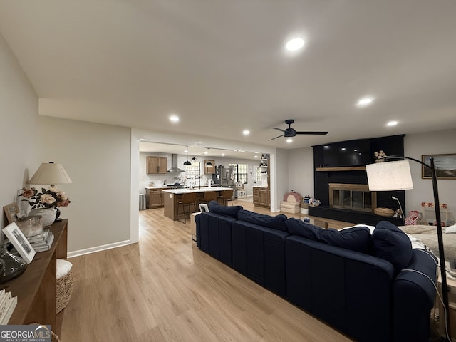 living room featuring a ceiling fan, light wood-style flooring, recessed lighting, a fireplace, and baseboards