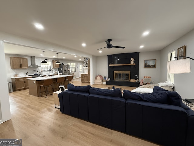 living room featuring ceiling fan, light wood finished floors, recessed lighting, and a brick fireplace