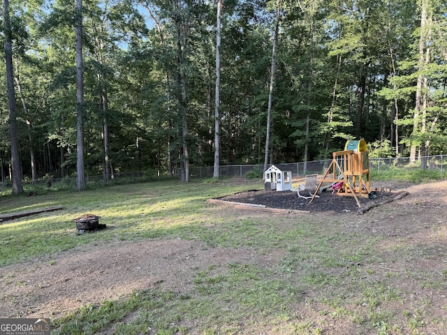 view of yard featuring a fire pit, a playground, and a forest view