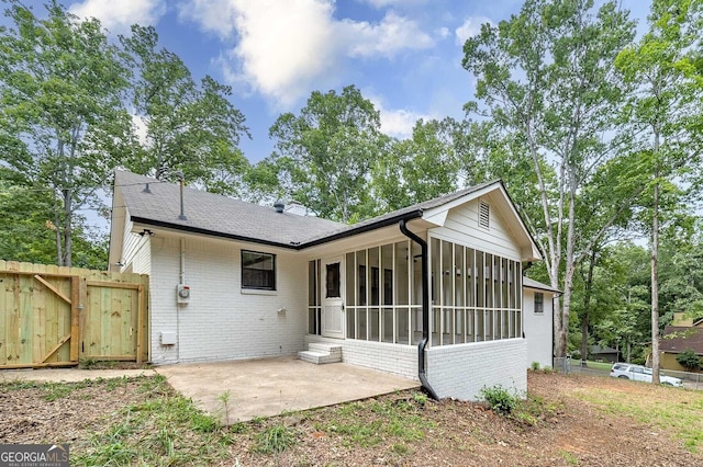 rear view of house with brick siding, a sunroom, a patio area, a gate, and a shingled roof