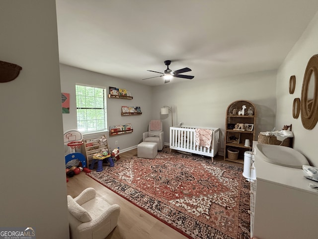 bedroom featuring a crib, wood finished floors, and a ceiling fan
