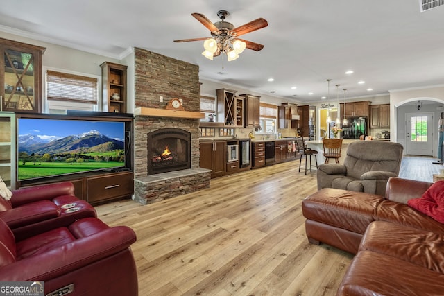 733 Firefly Ct, Griffin, GA 30223 - living room featuring crown molding, a ceiling fan, light wood-type flooring, arched walkways, and a stone fireplace