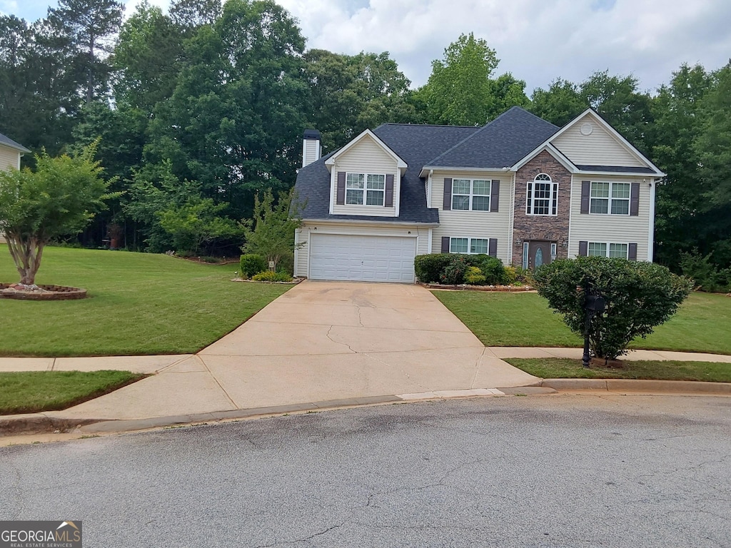 view of front of house featuring concrete driveway, a chimney, a front lawn, a garage, and view of wooded area