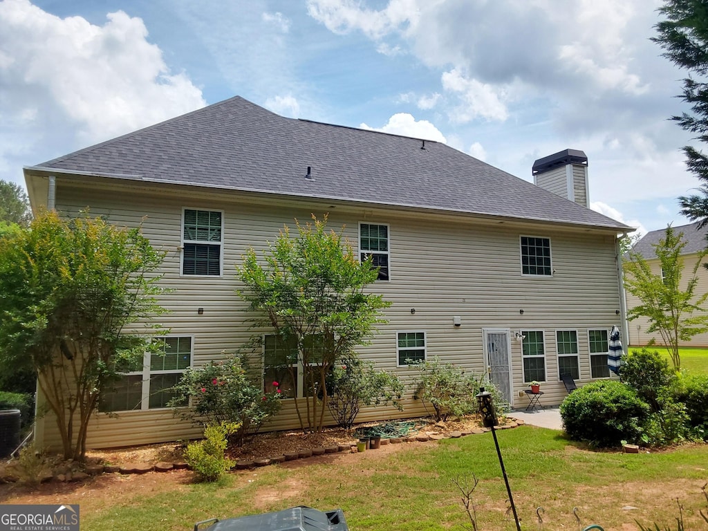 back of property with a chimney, a yard, a patio area, and a shingled roof