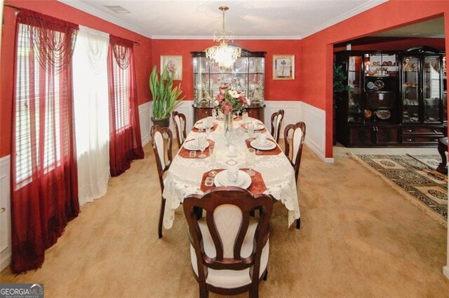 dining space featuring carpet flooring, a wainscoted wall, ornamental molding, and a chandelier
