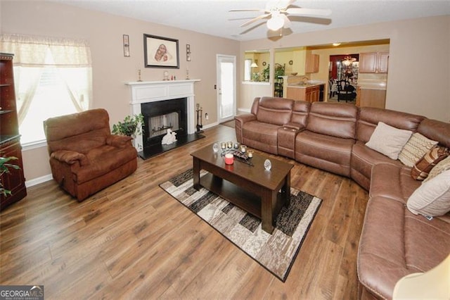 living room featuring ceiling fan, wood finished floors, baseboards, and a fireplace with raised hearth