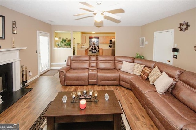 living room with ceiling fan, wood finished floors, a fireplace with raised hearth, and baseboards