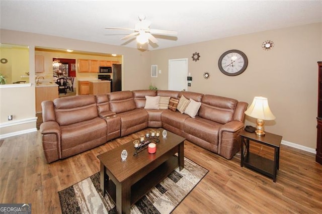 living room featuring light wood-style flooring, a ceiling fan, and baseboards