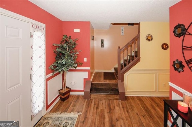 entrance foyer featuring stairs, wood finished floors, a textured ceiling, wainscoting, and a decorative wall