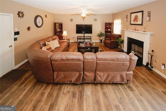 living area featuring ceiling fan, a fireplace, wood finished floors, and baseboards