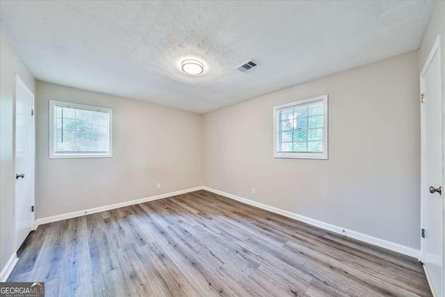 unfurnished bedroom featuring multiple windows, wood finished floors, baseboards, and a textured ceiling