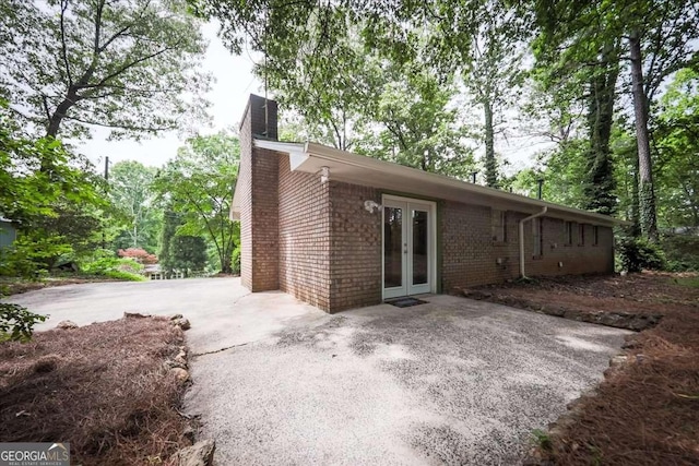 rear view of house with french doors, a chimney, and brick siding