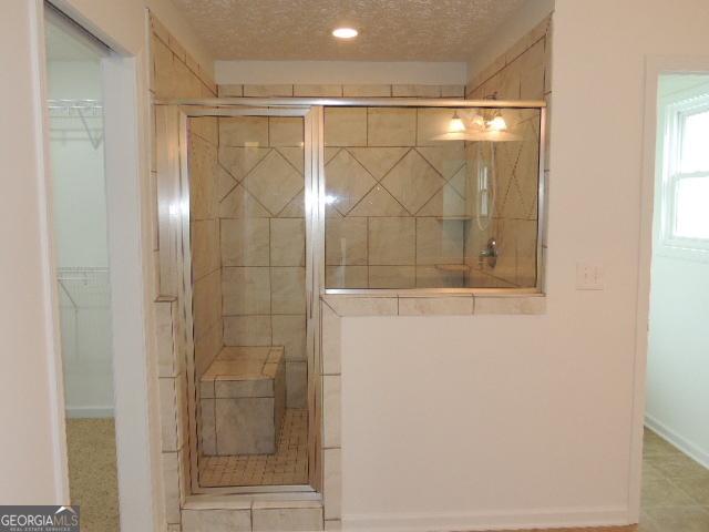 bathroom featuring a tile shower, a walk in closet, recessed lighting, a textured ceiling, and baseboards