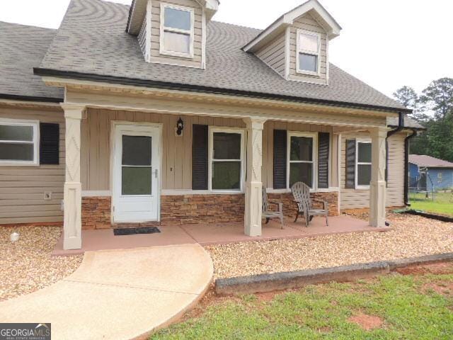 rear view of house with a porch, roof with shingles, stone siding, and board and batten siding