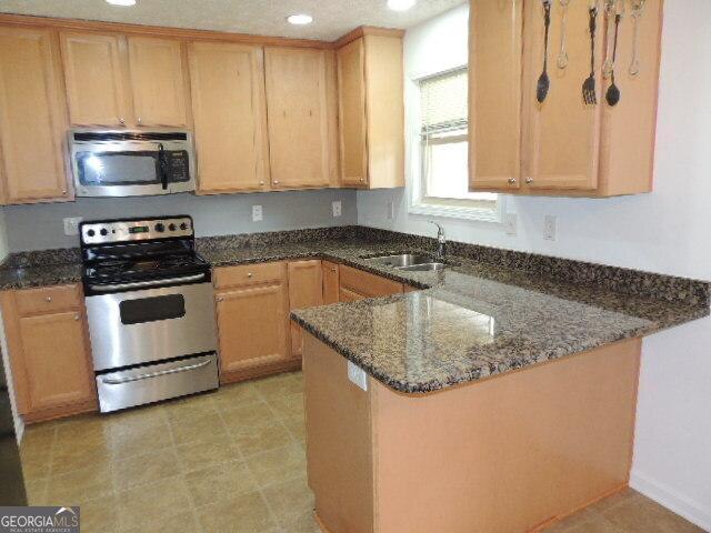 kitchen with stainless steel appliances, a peninsula, dark stone countertops, a sink, and recessed lighting