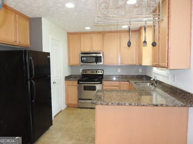 kitchen with appliances with stainless steel finishes, a sink, a peninsula, dark stone counters, and recessed lighting