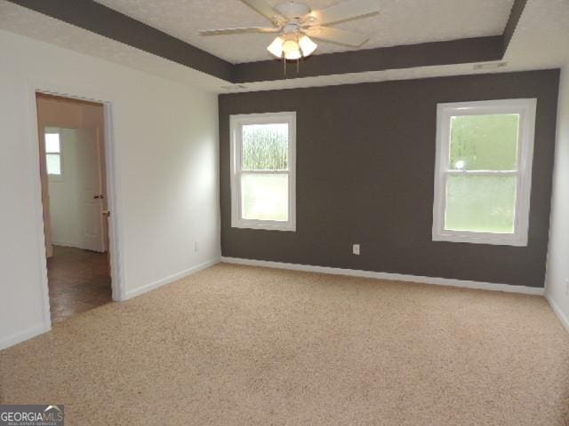 spare room with a raised ceiling, light colored carpet, baseboards, and ceiling fan