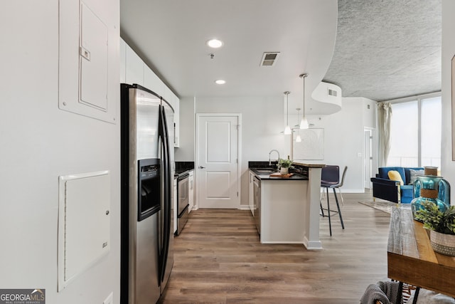 kitchen featuring dark countertops, stainless steel appliances, a kitchen bar, a sink, and white cabinets