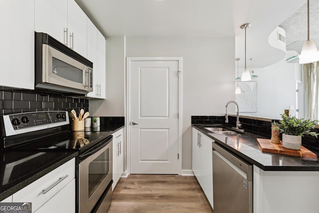 kitchen featuring appliances with stainless steel finishes, a sink, dark countertops, a peninsula, and light wood-style flooring