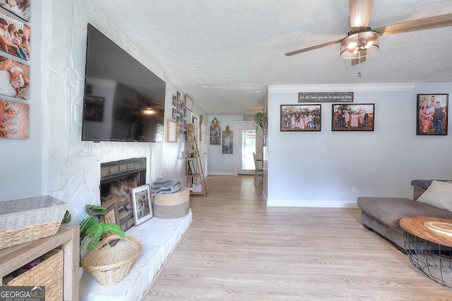 living area featuring wood finished floors, a fireplace, a ceiling fan, a textured ceiling, and baseboards
