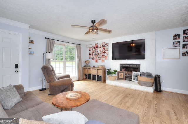 living area with ceiling fan, light wood-type flooring, a fireplace, a textured ceiling, and baseboards