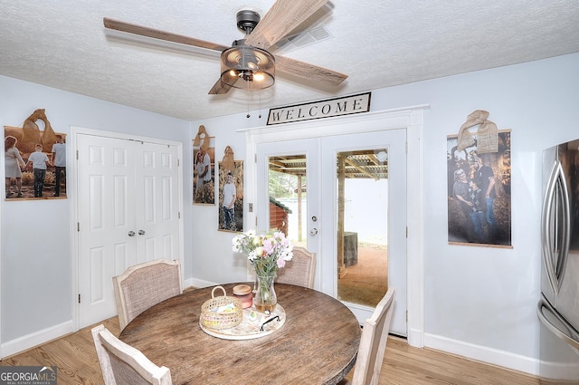 dining room featuring light wood-style floors, baseboards, french doors, ceiling fan, and a textured ceiling