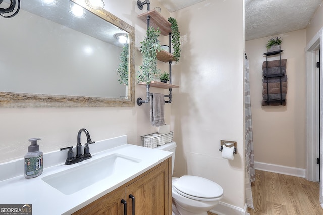 bathroom featuring wood finished floors, toilet, vanity, baseboards, and a textured ceiling