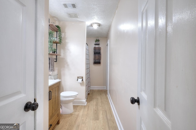 bathroom with toilet, wood finished floors, vanity, a textured ceiling, and baseboards