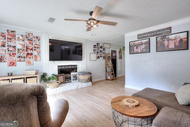 living area featuring ceiling fan, wood finished floors, a textured ceiling, a fireplace, and baseboards
