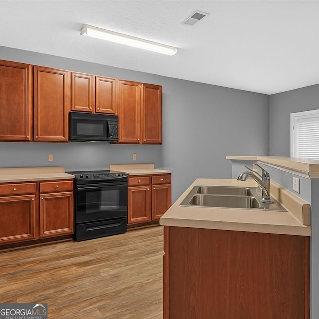 kitchen with black appliances, a sink, light wood-type flooring, and light countertops