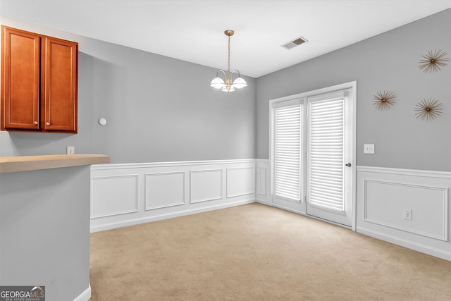 unfurnished dining area featuring light carpet, a wainscoted wall, a chandelier, and a decorative wall