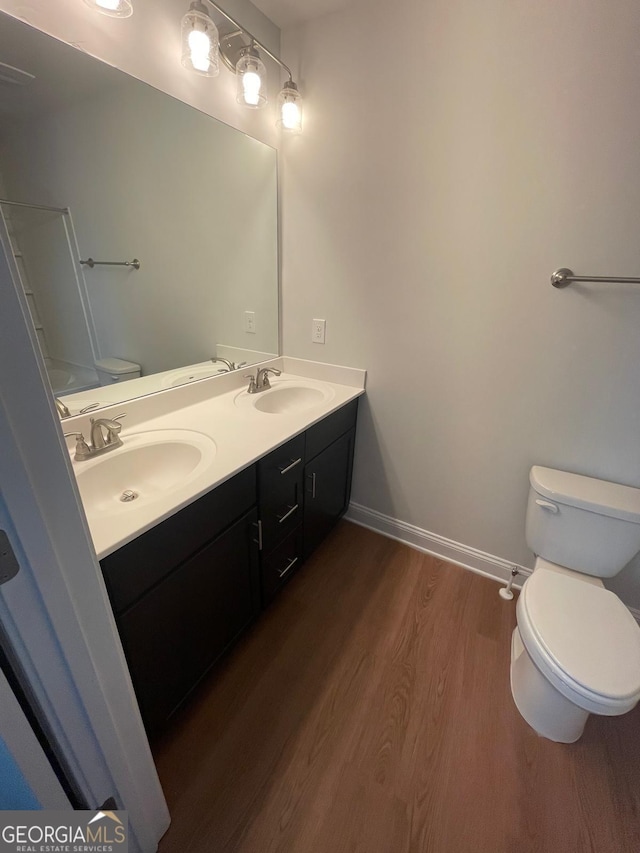 full bath featuring toilet, wood finished floors, double vanity, and baseboards