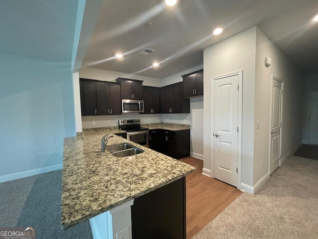 kitchen with appliances with stainless steel finishes, a sink, a peninsula, light stone countertops, and baseboards