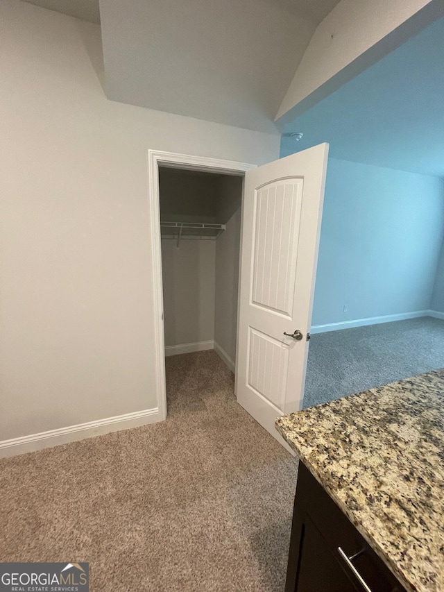 unfurnished bedroom featuring carpet floors, baseboards, a closet, and lofted ceiling