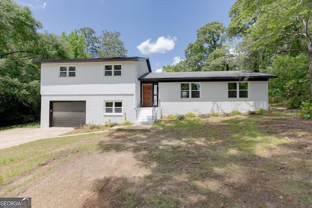 split level home featuring a garage, brick siding, and driveway