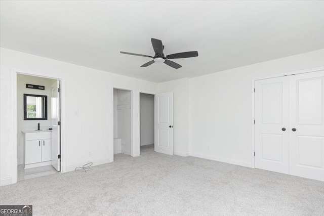 unfurnished bedroom with light colored carpet, a sink, ensuite bathroom, baseboards, and a ceiling fan