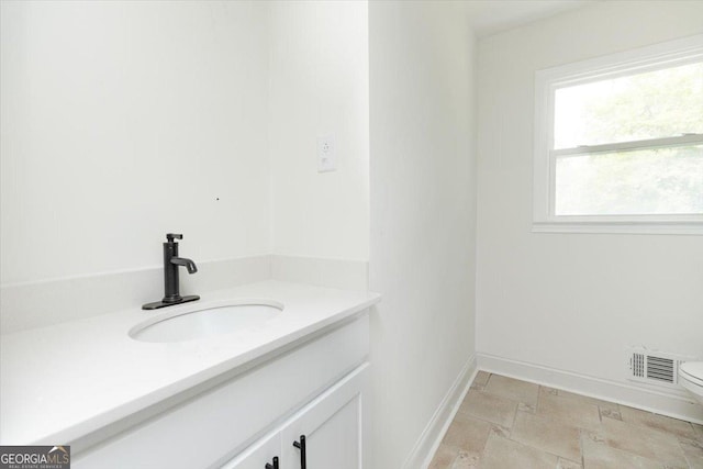 bathroom with vanity, toilet, baseboards, and stone finish flooring