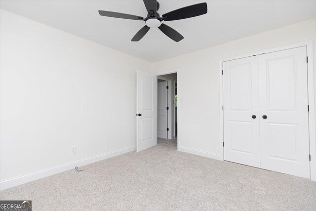 unfurnished bedroom featuring light colored carpet, baseboards, a closet, and a ceiling fan