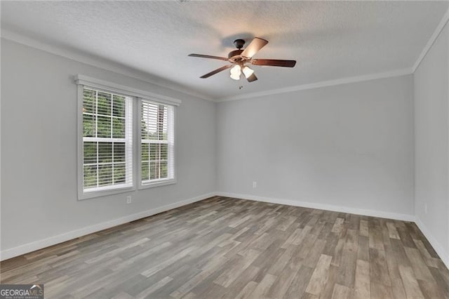 empty room featuring wood finished floors, ceiling fan, a textured ceiling, baseboards, and ornamental molding