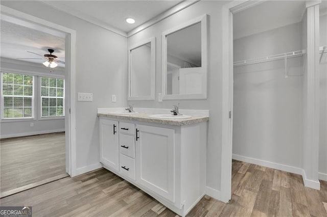 bathroom featuring a ceiling fan, wood finished floors, baseboards, double vanity, and a walk in closet